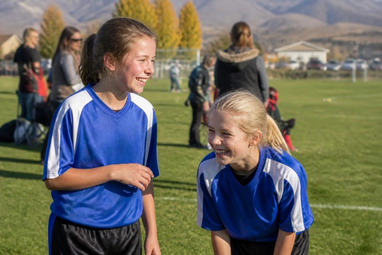 Two girls in soccer uniforms laughing on a youth soccer field